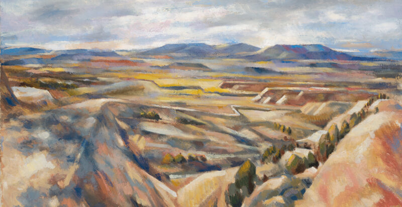 Landscape of sandy foothills with blue mountains in the background and a cloudy gray-blue sky