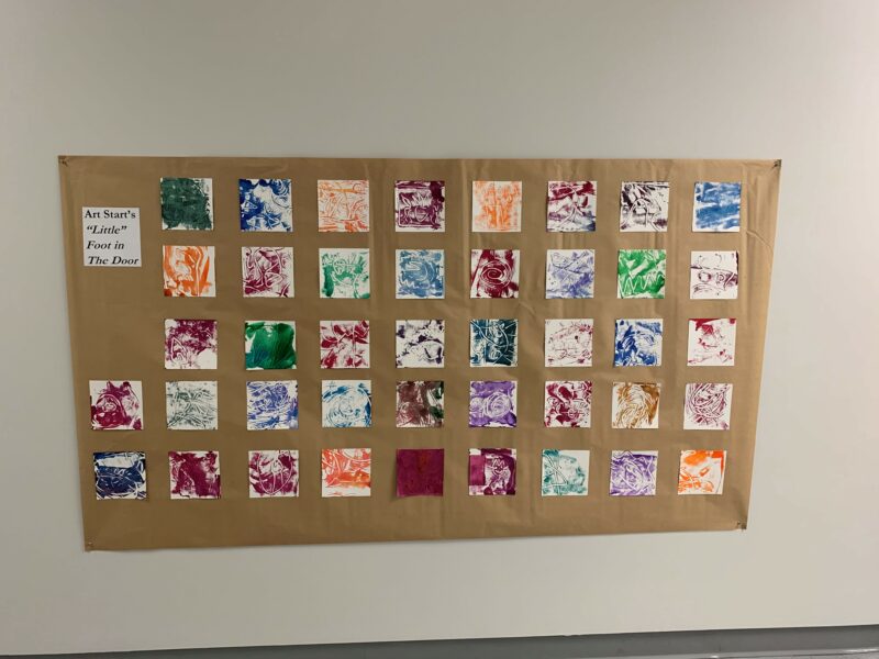 Photo of a series of 12 by 12 inch paintings on the wall arranged in a grid format