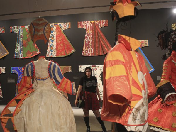 Museum visitor in the galleries stands near the tutus and with the kaftans in the background from the exhibition