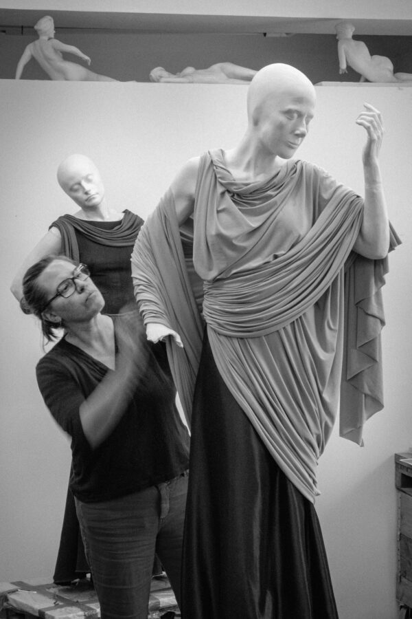 Photo of woman wearing glasses working with mannequins draped in fabric