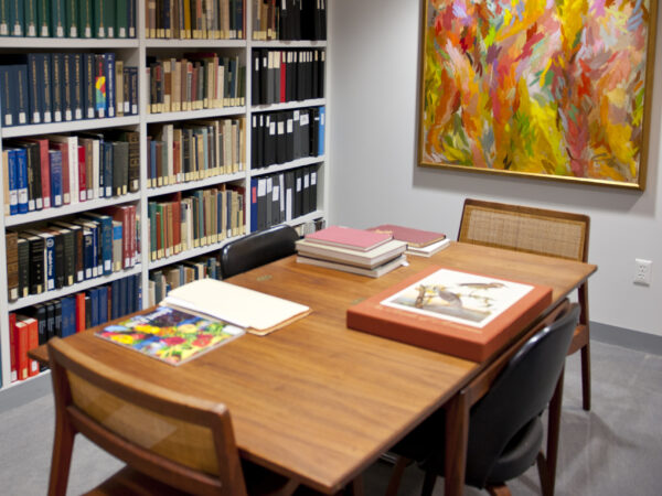 Interior view of the Library with a table and three chairs plus books on the table and bookshelves in the background