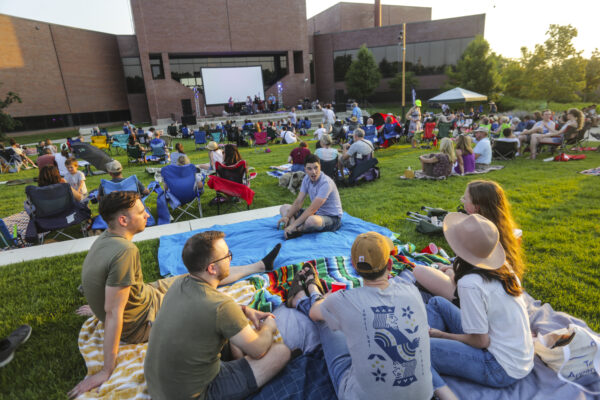 Groups of people wearing summer clothing sitting on the grass in the Art Garden